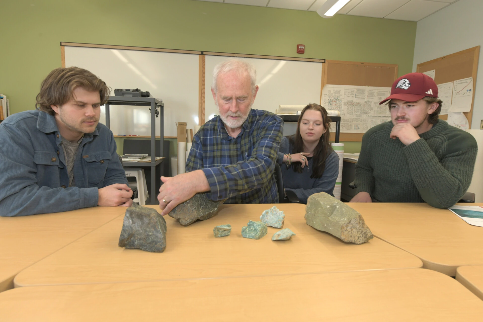 UMF students and professor sit at a desk studying rocks.