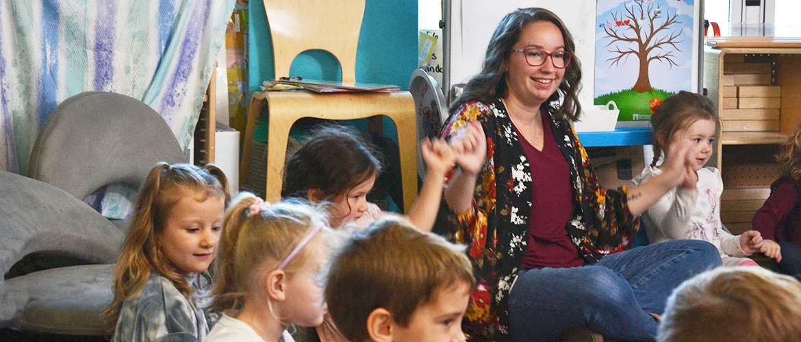 UMF education student sits and laughs with students in classroom.
