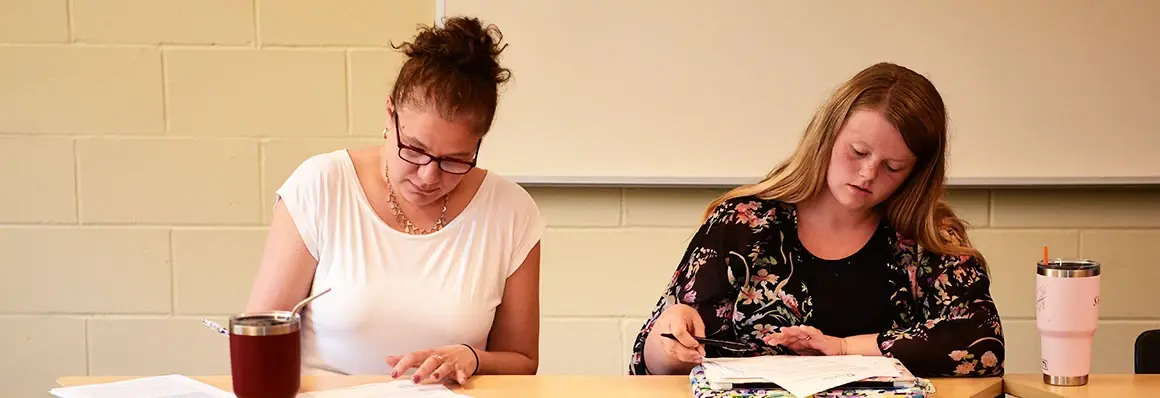 Professional writing students write at classroom desk.
