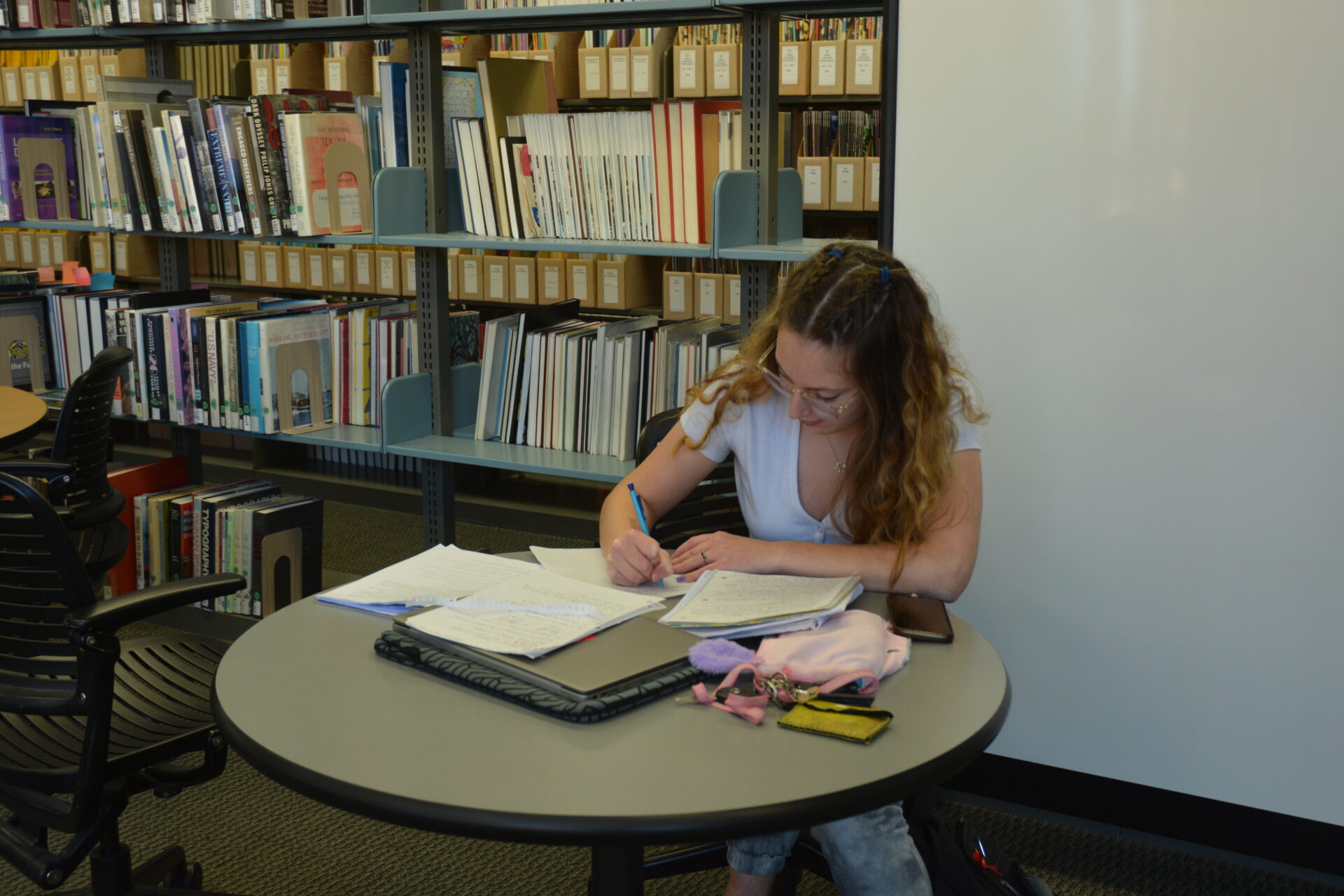 Student working at table in library writing in notebook.