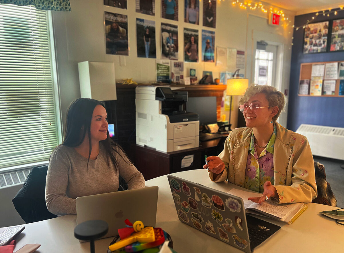 Two students sitting and talking while working on their laptops