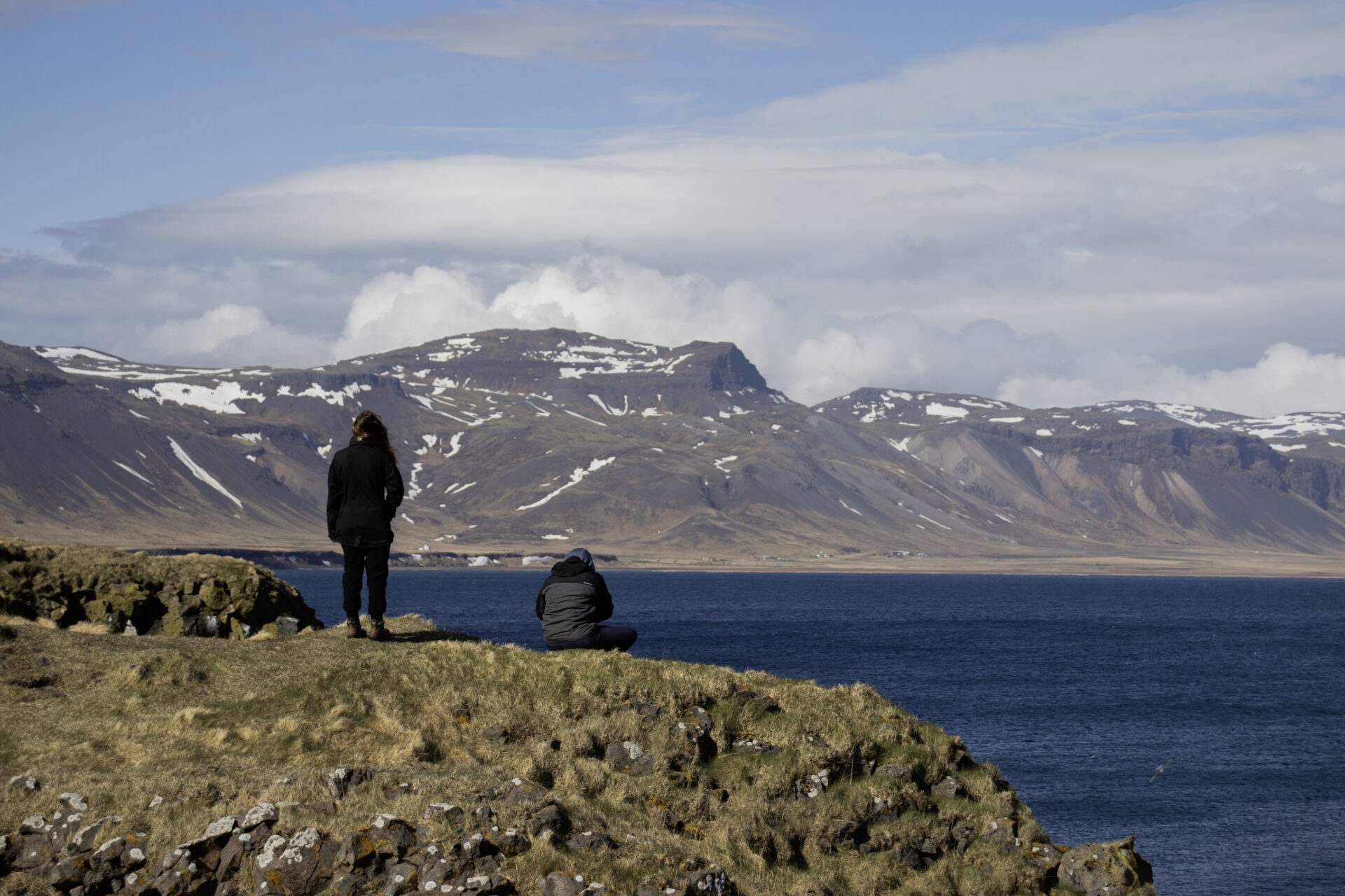 Two students sitting on a rocky beach looking out at the sea in Iceland.